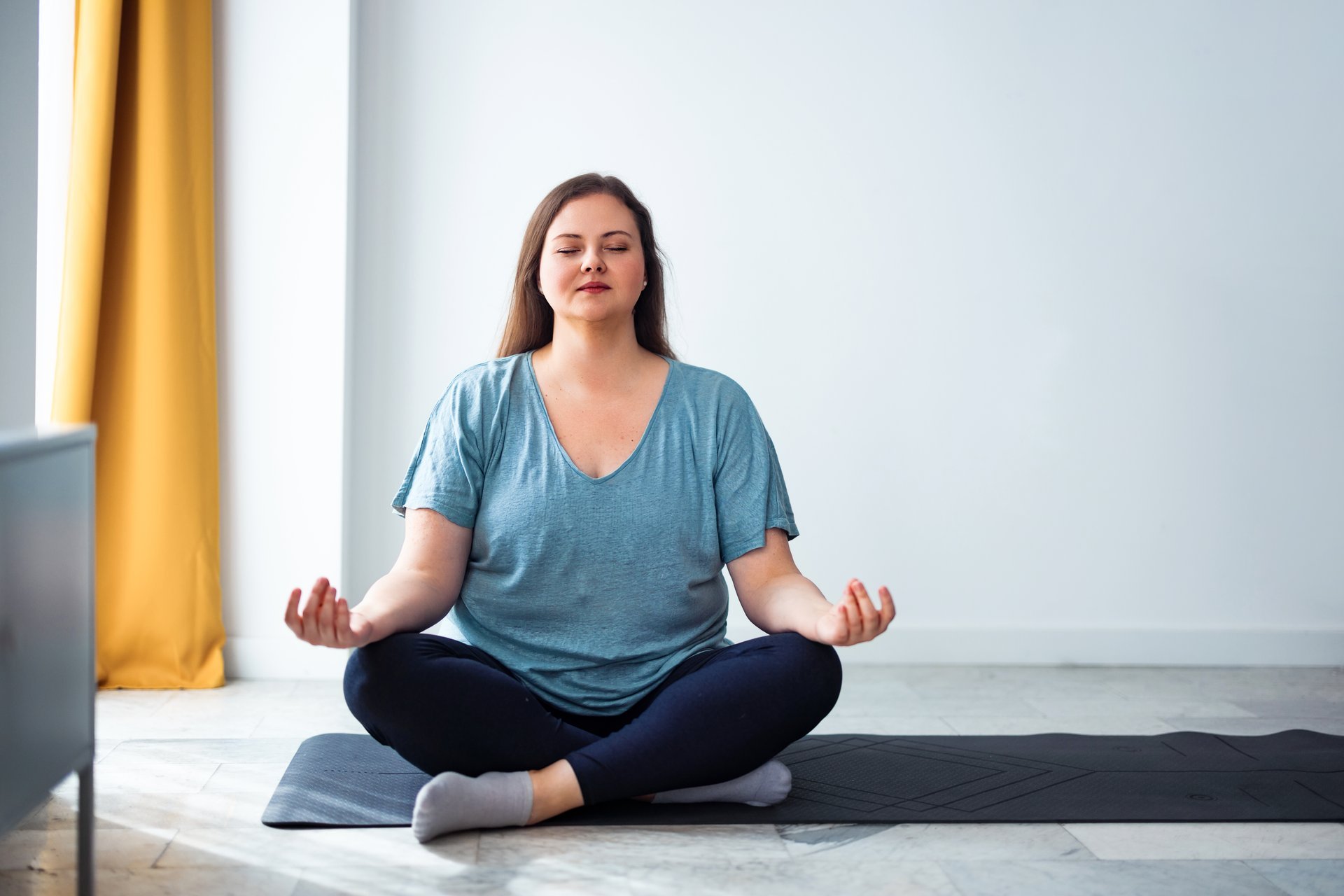 Woman practicing meditation while seated in cross-legged pose indoors enjoying calmness