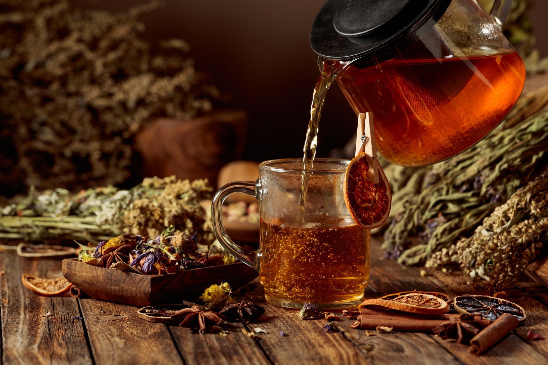 Hot herbal tea poured into a glass mug with dried herbs on wooden table
