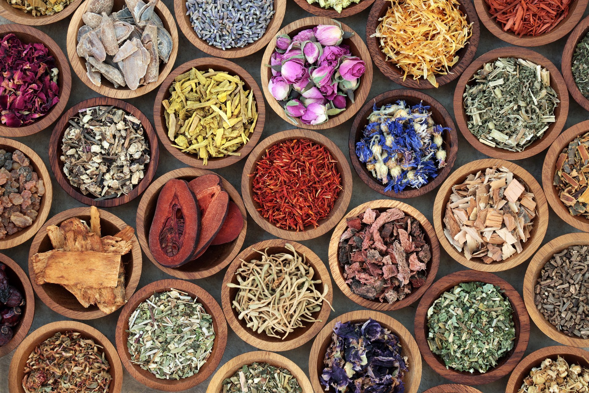 Assorted dried medicinal herbs and flowers in wooden bowls on rustic table